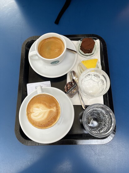 Kaffee-Tablett mit zwei Tassen Kaffee, zwei Patisseriestückchen und zwei Gläsern Wasser, die es umsonst dazu gab.