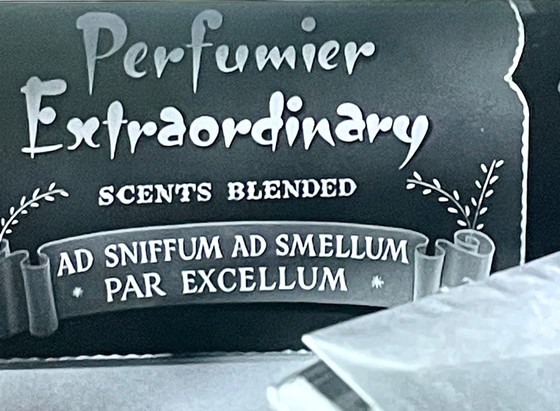 Firmenschild eines Parfumeurs, der in einer Szene der Episode eine wunderbar skurrile Nebenrolle spielt:
Perfumier Extraordinary
SCENTS BLENDED
AD SNIFFUM AD SMELLUM PAR EXCELLUM