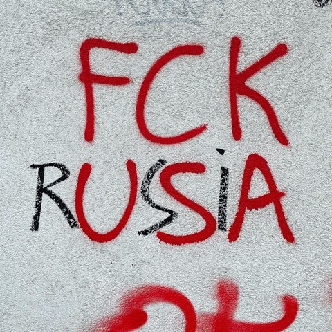 Graffiti an einer hellen Hauswand: in die Zeichenzwischenräume der ursprünglich in rot aufgesprühten Parole FCK USA wurden in schwarz die Lettern R, S und I eingefügt. Ergebnis: FCK RUSSIA