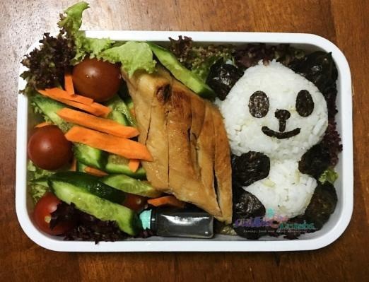 Japanische Zubereitung einer Bento Box für Kinder mit einigen Reisbällchen, die mit Nori Tang zu einer niedlichen Panda-Figur geformt sind 