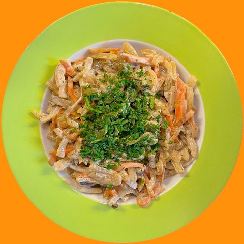 Ein grün-weißer Teller auf orangefarbenem Hintergrund, von oben fotografiert. Darauf eine große Portion des benannten Salates, bestreut mit gehackten Kräutern.