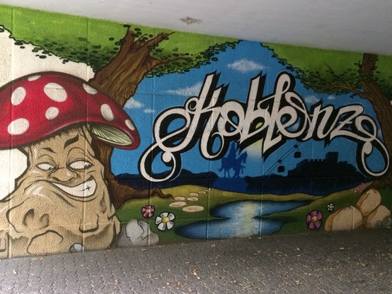 Buntes Wandgraffiti einer skurrilen Figur unter einem roten Pilz mit dem Wort 