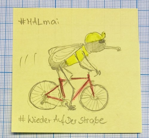Hand-drawn sketch of a fly cycling on a pink bike, wearing a yellow cap and shirt, on a yellow sticky note with grid lines in the background and hashtags #MAlmai and #WiederAufDerStraße written on it.