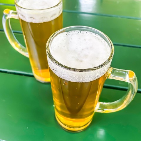 Zwei frisch gezapfte 0,3l-Humpen Bier auf einem grün lackierten Holztisch 