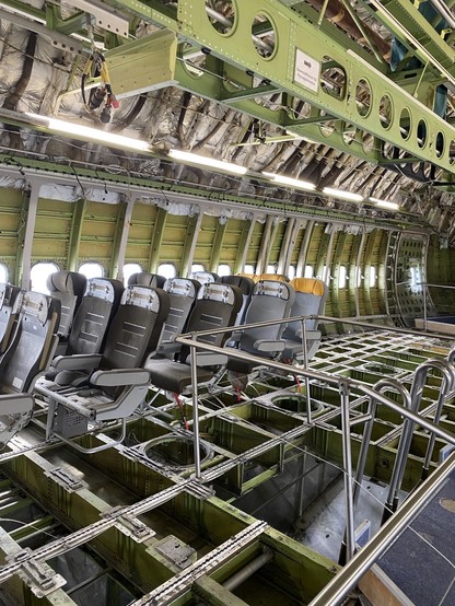 Interior of an aircraft under assembly or maintenance, showing exposed frame and some passenger seats installed.