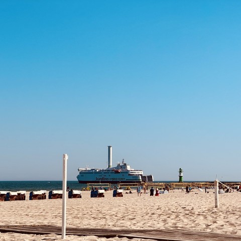 Fährschiff Copenhagen ausgehend mit dem charakteristischen Rotorsegel, hinter der Fähre das grüne Molenfeuer, davor am Strand ein Beachvolleyball-Turnier