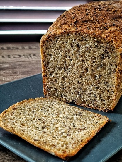 Tin loaf of bread, with one slice cut off, showing the fine poring of the crumb and tiny specks of quinoa seed