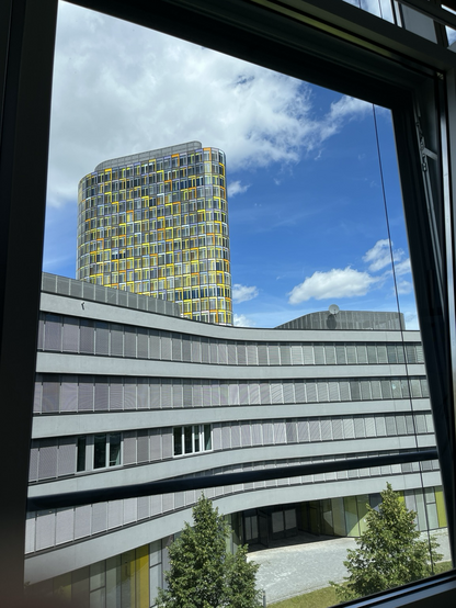 Blick durch Bürofenster auf modernes Büro-Hochhaus vor blauem Himmel 