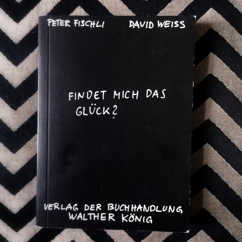 Peter Fischli/David Weiss: Findet mich das Glück? Ein schwarzes Buch mit weißer Schrift auf grau-weißem Hintergrund 
