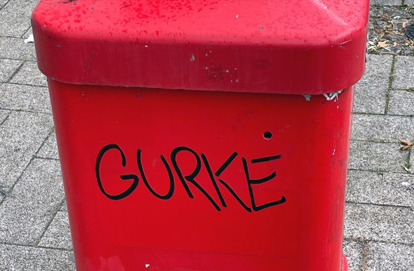Aufnahme eines knallroten öffentlichen Abfallbehälters auf einem Hamburger Gehsteig, darauf mit dickem schwarzen Marker der Schriftzug GURKE