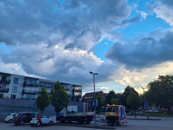 Dräuende Wolken, quaderförmiges Gebäude,  Fahrzeuge auf Parkplatz 