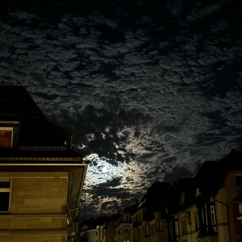 Der Mond scheint durch die nächtliche Wolkendecke, die Wolken sind kleinteilig zerrupft und an einigen Stellen etwas dicker, das durchscheinende Mondlicht verstärkt die Kontraste.