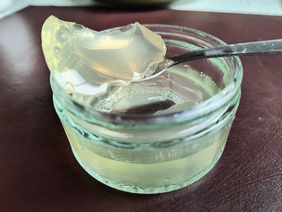 Löffel mit Götterspeise, der auf einem Glas halb gefüllt mit hellgrüner Götterspeise Geschmacksrichtung Mojito liegt