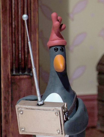Szenenbild aus dem Animationsfilm Wallace und Gromit – Die Techno-Hose: Der böse Pinguin Feathers McGraw mit Fernbedienung in den Händen, mit der er die Roboterhose steuert, in der Wallace steckt. 