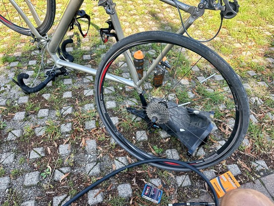 Ein silbernes Rennrad steht kopfüber und das hintere Rad ist ausgebaut, mit entferntem Schlauch. Daneben Werkzeug und Ersatzschlauch