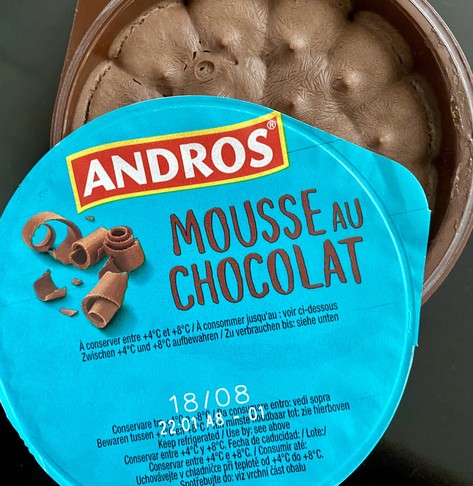 Eine tiefgefrorene vegane Mousse au Chocolat. Der Deckel der Verpackung liegt versetzt auf dem Rand der Schale, so dass man die Mousse sehen kann.