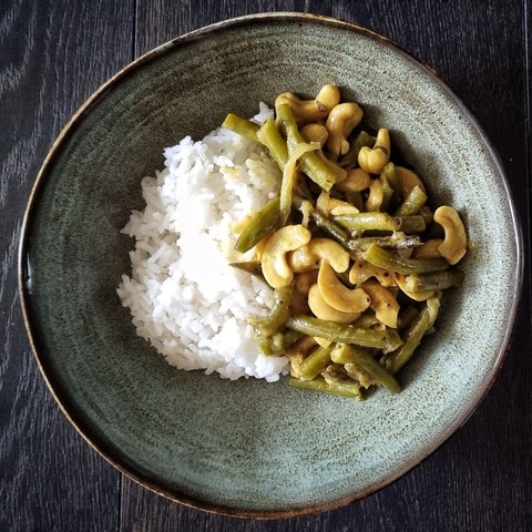 a greenish earthenware bowl with rice and a curry with short pieces of green beans and cahsew nuts on the side