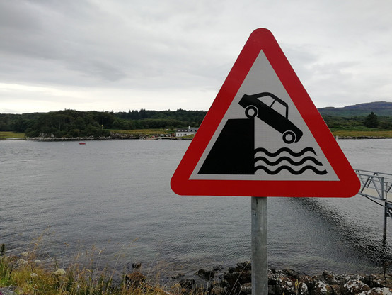 a warning sign at a sea loch, depicting a car falling into water