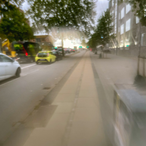 Foto entlang der rechten Straßenseite einer Stadtroute in Kopenhagen-Valby. Von links nach rechts erkennt man baulich getrennte, angenehm breite Bereiche/Spuren für fahrende Autos, Parkende Autos, Radfahrer und Fußgänger.