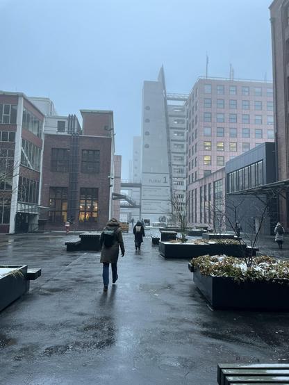Personen bewegen sich durch nebligen Niesel zu ihren Büros in der Ullsteinstraße.