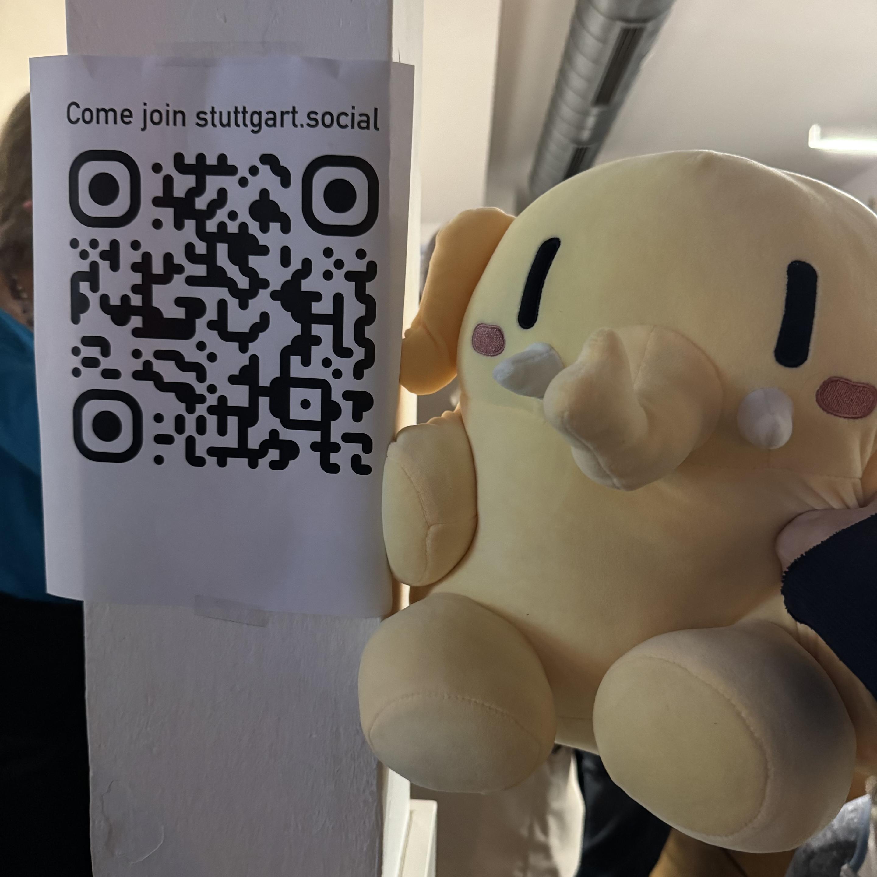 Ein Plushtodon neben einem QR-Code des Einladungslinks, der auch im Post steht.