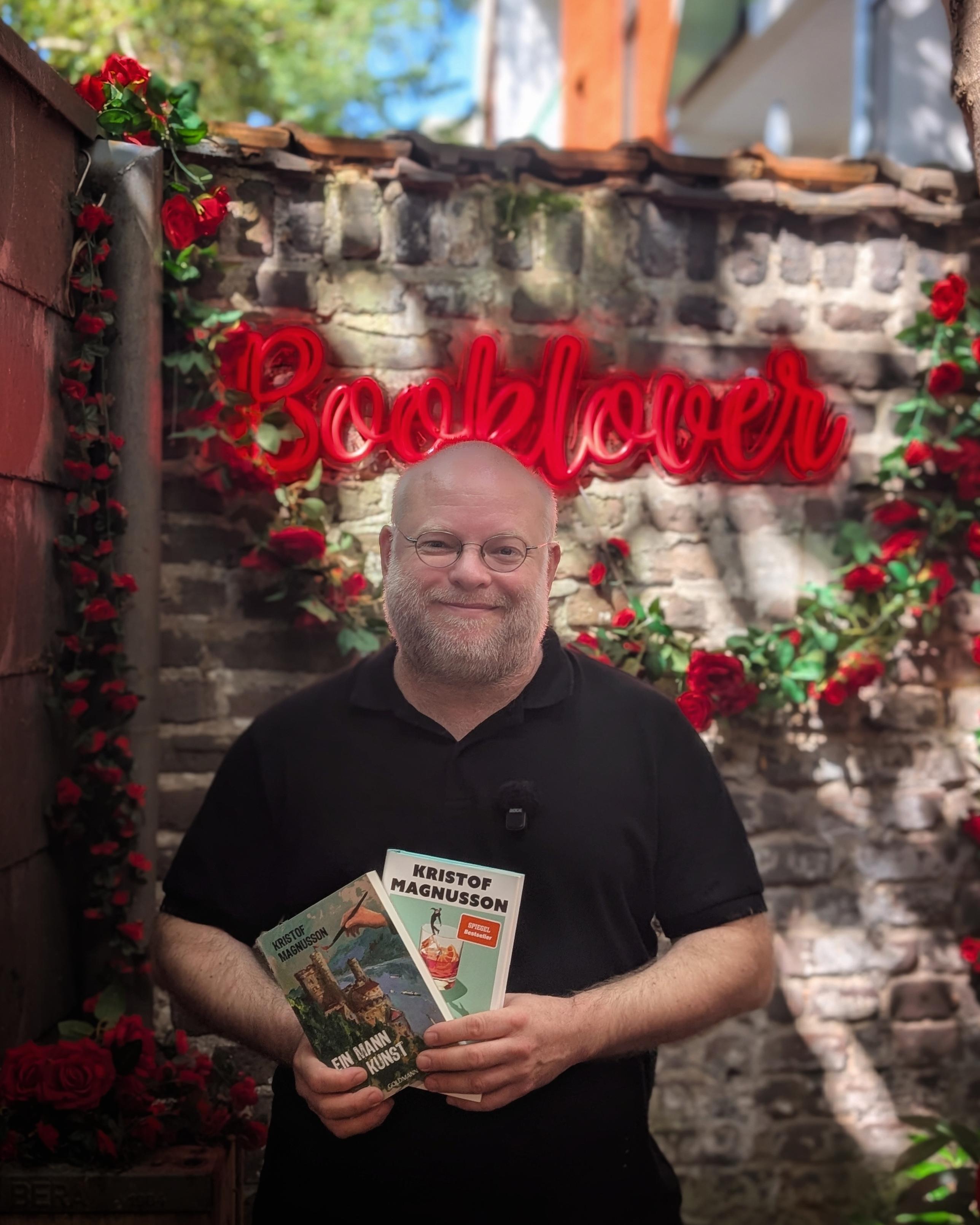 Kristof Magnusson in unserem Rosengarten mit dem Neonschriftzug "Booklover" im Hintergrund