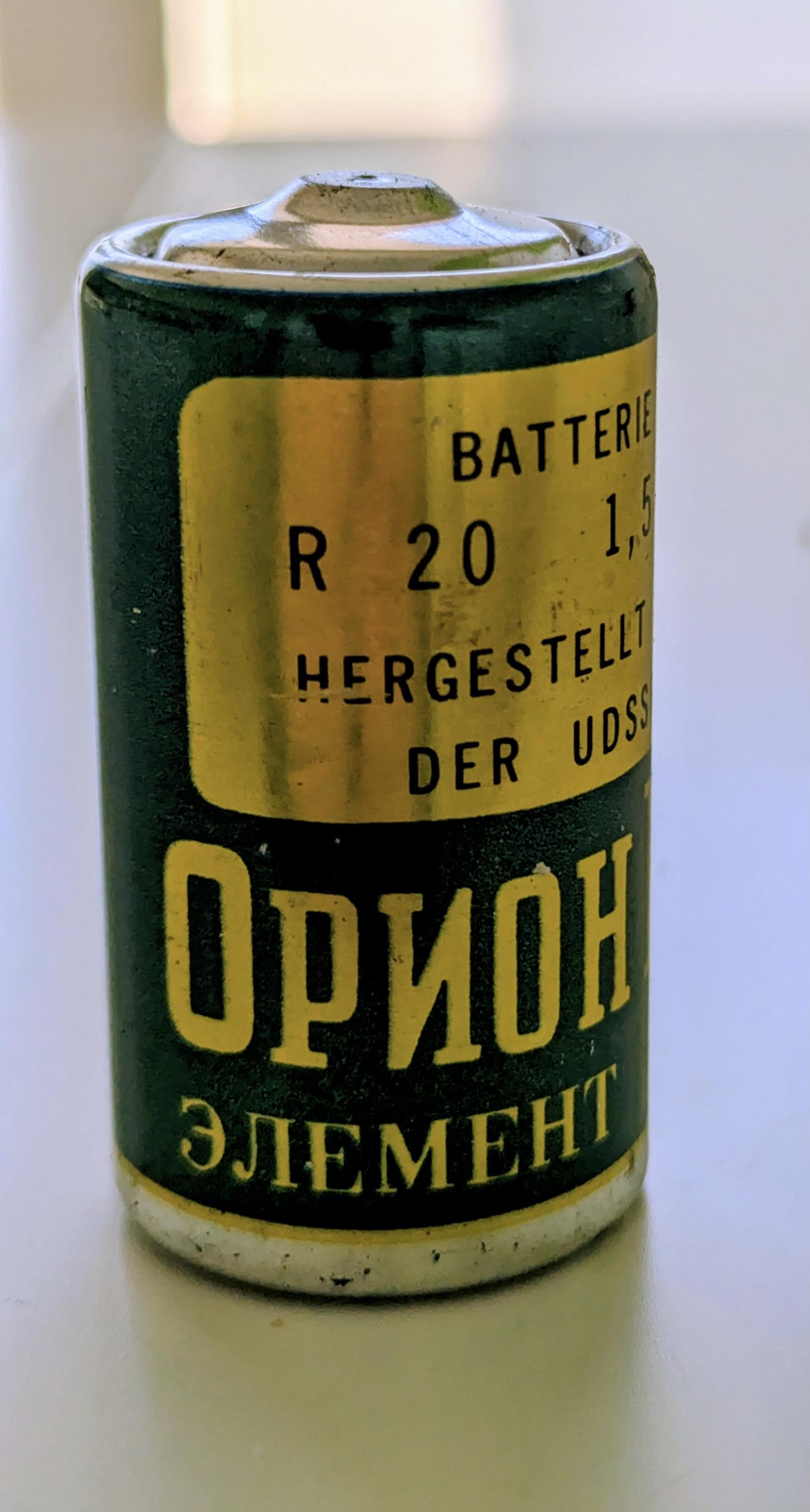 Sehr alte dicke R20 Batterie in grün-gold mit Aufdruck:
Batterie 
R20   1,5V
Hergestellt in der UDSSR
(nun in kyrillischen Buchstaben:)
Orion M
Element 373